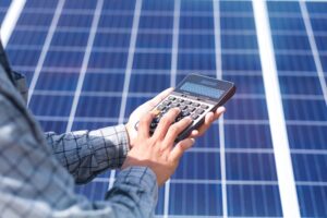 Hand holding calculator and checking solar panel maintenance cost